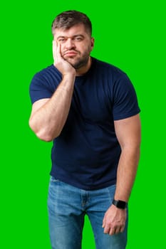 Young man with a contemplative expression leaning against green backdrop while resting his head on his hand in studio