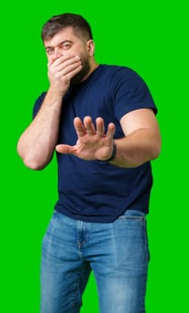 A man with a serious expression holds up both hands in a stopping gesture against a bright green background in studio