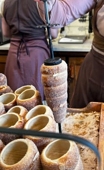 Pastry chef baking a kurtos kalacs, a traditional hungarian sweet pastry, sprinkling it with sugar and chopped almonds
