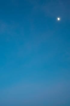 Clear blue sky with a visible crescent moon, creating a serene and unique daytime scene