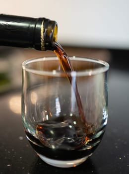 Red wine pouring from a bottle into a glass, creating a splash on a dark, reflective surface