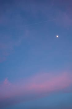 Airplane leaving contrail in colorful sunset sky with moon
