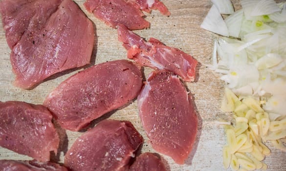 Seasoned pork tenderloin, chopped onions, and minced garlic arranged on a wooden cutting board, ready for cooking