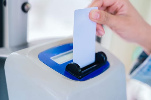 Close-up of a hand inserting a ticket into a validation machine on public transport. The electronic device scans the ticket for access. Modern commuting and transportation system concept.