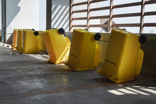 Bangkok, Thailand - Jan 18, 2025 -  Perspective view of Plastic trash with lid for general waste and turn upside down to dry near concrete wall on parking lot of condominium building. Yellow large plastic rubbish bins After cleaning big plastic yellow garbages container, use it as your wallpaper, poster and Copy space, selective focus.