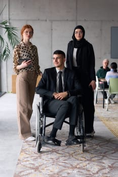 A diverse business team poses confidently, including a smiling director seated in a wheelchair, flanked by two professional female colleagues, one wearing a hijab and the other holding a tablet, in a modern office environment.