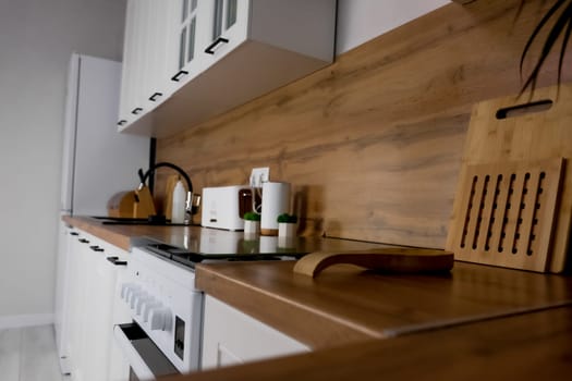 View of the modern kitchen from the side table, white cabinets and wooden countertop, gas stove and white refrigerator, black sink and plants. Modern Kitchen, Kitchen Island, Kitchen Design Concept. High quality photo