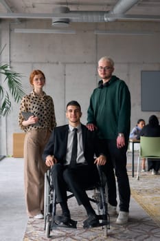 Group cheerful business colleagues, including a businessman in a wheelchair, posing together in a modern office, showcasing teamwork and inclusivity.