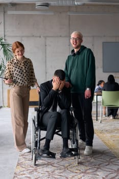 Group cheerful business colleagues, including a businessman in a wheelchair, posing together in a modern office, showcasing teamwork and inclusivity.