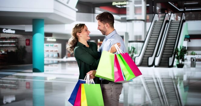 Family With Bags In Shopping Mall. Happy Man And Woman Buying Fashion