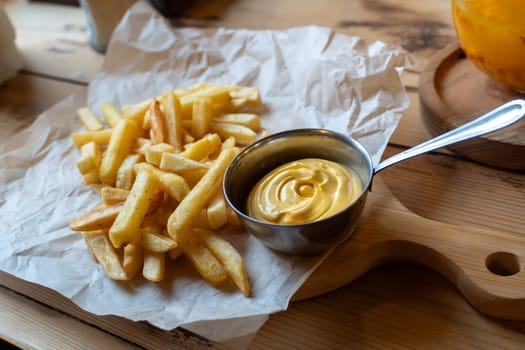 Crispy french fries with creamy mayonnaise on wooden board.