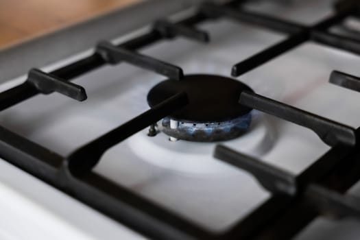Close-up of a white gas stove with a black cast-iron grate and a black burner on which a blue fire burns. Gas stove, cooking concept. High quality photo