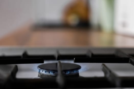 Close-up of a white gas stove with a black cast-iron grate and a black burner on which a blue fire burns against the background of a wooden kitchen in out-of-focus. Gas stove, cooking concept. High quality photo
