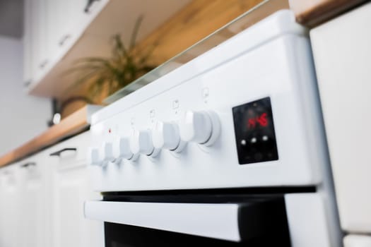 Close-up in focus panel with rotary control knobs at kitchen white gas stove against wooden countertop background and white cabinets of modern kitchen out of focus. Concept of cooking, temperature control, cooking modes. High quality photo