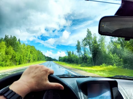 Car salon, windshield, hand of woman on steering wheel and landscape. View from seat of driver on nature with Road, tree and blue sky at sunny day