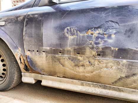 A damaged car's side shows signs of wear and tear, with scraped paint and rust visible.