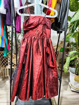 A striking red dress hangs at a garage sale, showcasing second-hand clothing with an emphasis on environmental sustainability.