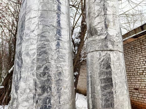 Silver insulation wraps heat pipes to prevent freezing in a chilly outdoor setting, showcasing winter's impact on infrastructure.