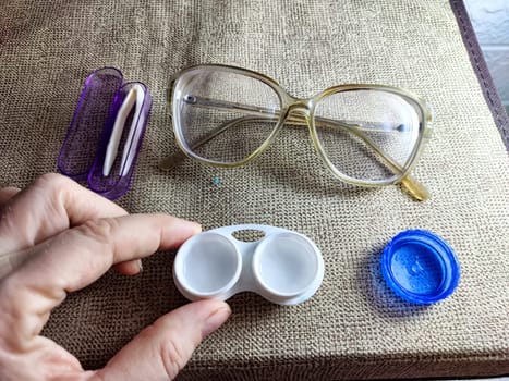 Close-up of essential contact lens care items including a lens case, cleaning solution, and spectacles placed on textured fabric.
