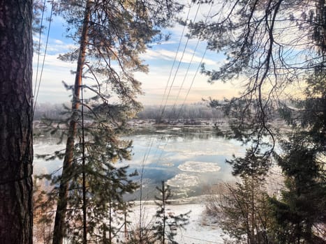 Snow and ice fragments break away in the river at early morning as spring begins, surrounded by tall trees and soft light.