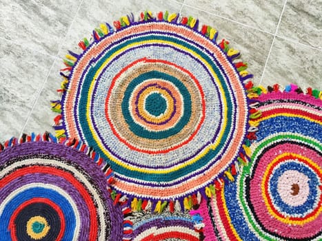 Vibrant circular rugs with intricate designs and fringes are arranged on a textured floor, showcasing their colorful craftsmanship and patterns.