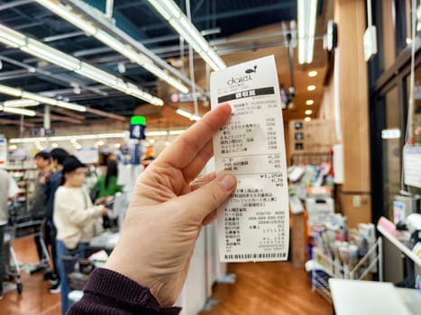 Osaka, Japan - October 25, 2024: A hand holds a receipt detailing purchases at a store in Osaka, Japan, surrounded by other shoppers and store displays.
