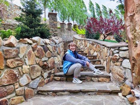 A woman enjoys her adventure trip as she takes a moment to relax on stone steps amid lovely greenery and flowers.