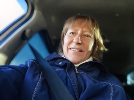 A middle aged woman smiles warmly in her car, capturing a moment of joy during a sunny road trip adventure.