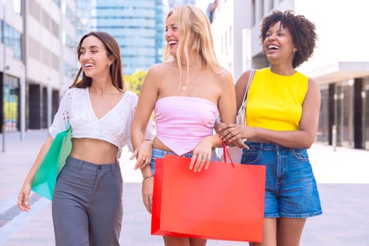 Three young women enjoying a sunny day, carrying shopping bags and smiling as they walk in an urban environment. Perfect for concepts like friendship, shopping, fashion, and lifestyle.
