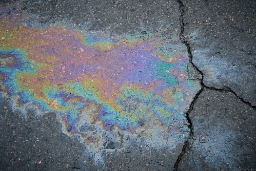 Gasoline or oil spill creating rainbow colors on cracked asphalt road.