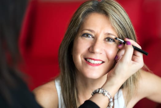 Beautician applying makeup to a smiling friendly happy female model using a fine brush to apply cosmetics or eye shadow to the eye