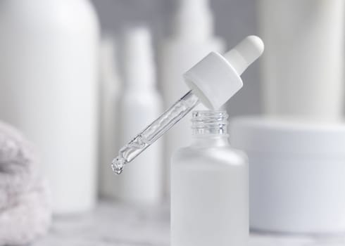 Drop falls from a pipette set on trasparent glass dropper bottle against cosmetics in bathroom closeup. Natural organic serum or essence or for beauty routin