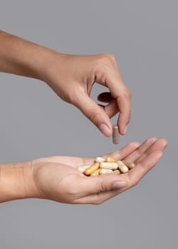 Female hand taking one beige medical capsule with fingers and holding others in a cupped hand against grey, closeup, negative space. Alternative herbal products for health care