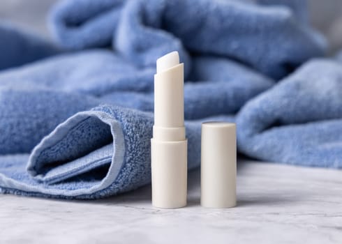 Opened white blank lip balm stick near blue bath towel, top view, cosmetic mockup. Lifestile scene with Lipcare beauty product for mens daily personal care