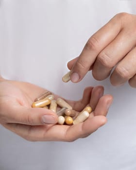 Woman holding in hands beige medical capsules over white shirt and taking one capsule with fingers closeup, cropped shot. Alternative herbal products for health care