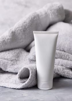 White blank cosmetic squeeze cream tube near light grey towel in bathroom top view, brand packaging mockup. Natural herbal cosmetic product for daily facecare, copy space