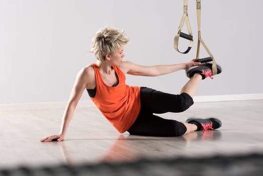 Single woman in orange sleeveless shirt placing training rings around feet while sitting on hardwood floor
