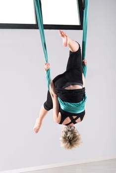 Upside down woman performing an aerial yoga somersault while suspended from ceiling with green cloth