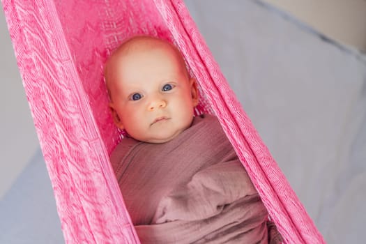 A 3-month-old baby peacefully falls asleep in a soft muslin swaddle while cradled in a cozy hammock. A serene and tender moment of comfort and relaxation. Baby care, rest, and tranquility concept.