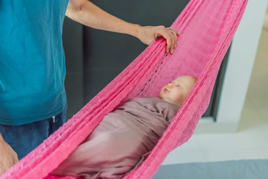 A 3-month-old baby peacefully falls asleep in a soft muslin swaddle while cradled in a cozy hammock. A serene and tender moment of comfort and relaxation. Baby care, rest, and tranquility concept.