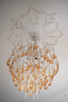 crystal chandelier on the ceiling. the chandelier is beautiful, rich, with crystals. the crystal is golden and white. there is antique stucco on the ceiling