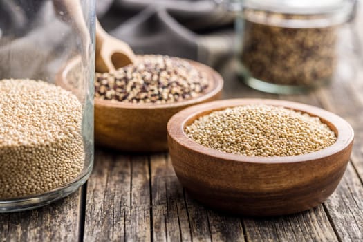 Mixed uncooked quinoa seeds in bowl on a wooden table.