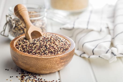 Mixed uncooked quinoa seeds in bowl on a white table.