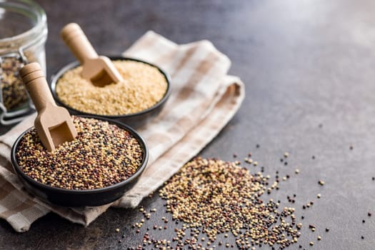 Mixed uncooked quinoa seeds in bowl on a black table.