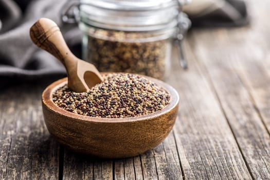 Mixed uncooked quinoa seeds in bowl on a wooden table.