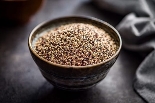 Mixed uncooked quinoa seeds in bowl on a black table.