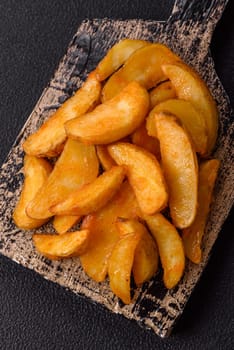 Baked potato wedges with cheese and herbs on a dark background. Homemade organic vegetable vegan vegetarian potato wedges