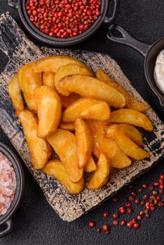 Baked potato wedges with cheese and herbs on a dark background. Homemade organic vegetable vegan vegetarian potato wedges