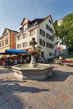 Meersburg, Germany – August 03, 2024: Historical fountain, Brunnen des Altertum and tourists at a wine tavern in Meersburg on Lake Constance, Bodensee in Germany
