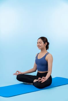 Asian woman in sportswear doing yoga exercise on fitness mat as her workout training routine. Healthy body care and calm meditation in yoga lifestyle in full body shot on isolated background. Vigorous